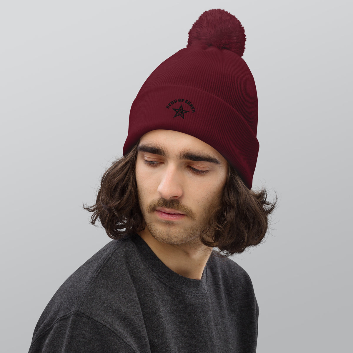 Man met een pom pom beanie in bordeauxrood, ideaal voor koude dagen en een comfortabele pasvorm.